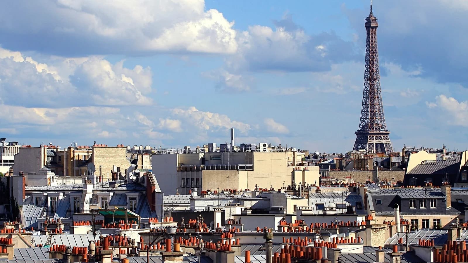 Toits de Paris sous un ciel bleu nuageux, avec la tour Eiffel à l’horizon