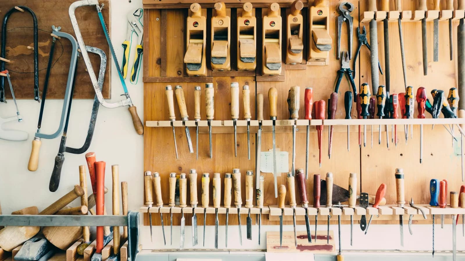 Un mur d’atelier en bois où sont rangés avec soin rabots, ciseaux à bois, tournevis, scies et pinces.
