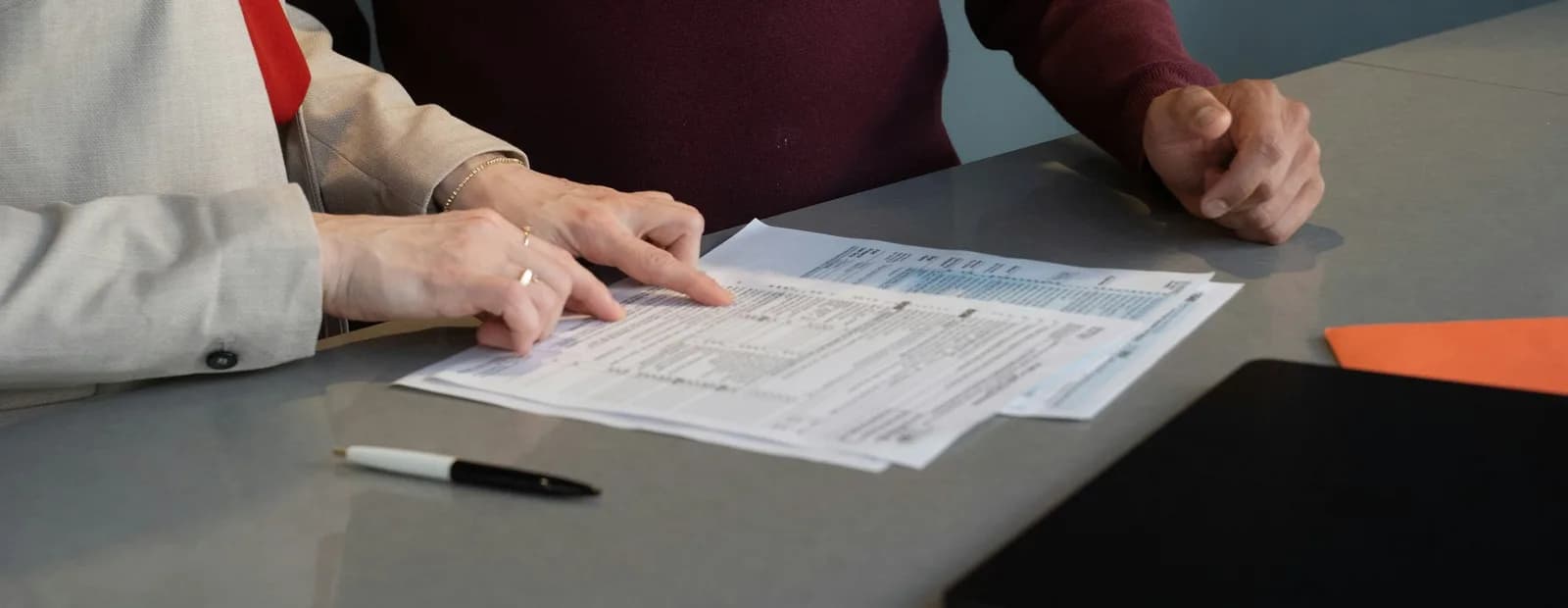 Deux collègues penchés sur des documents posés sur une table grise, cadrés à hauteur des mains.