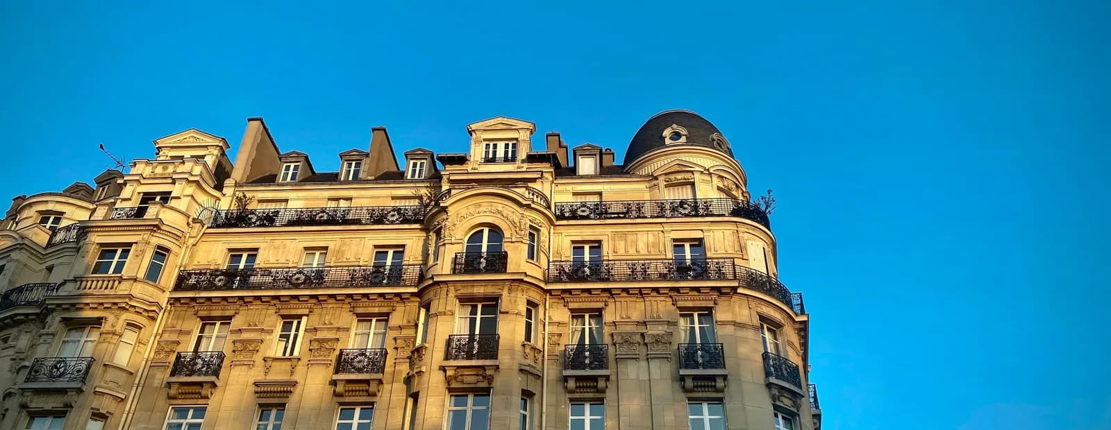 Immeuble haussmannien à balcons en fer forgé, éclairé par un soleil rasant sous un ciel bleu profond