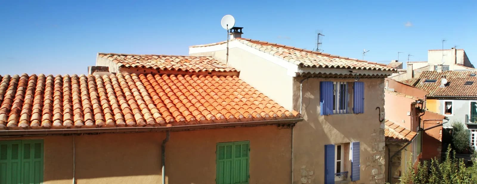 Maisons aux toits de tuiles et aux volets bleus et verts du village de Ventabren, voisin d’Éguilles, sous un ciel bleu.