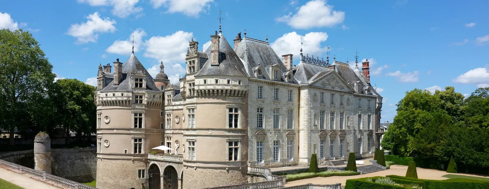 Château du Lude en pierre de tuffeau claire, tours Renaissance et façade classique, jardins à la française et arbres centenaires sous un ciel bleu.
