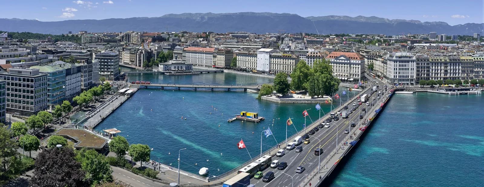 Vue aérienne de Genève : un pont routier franchit l’eau entre le lac et la ville, montagnes à l’horizon