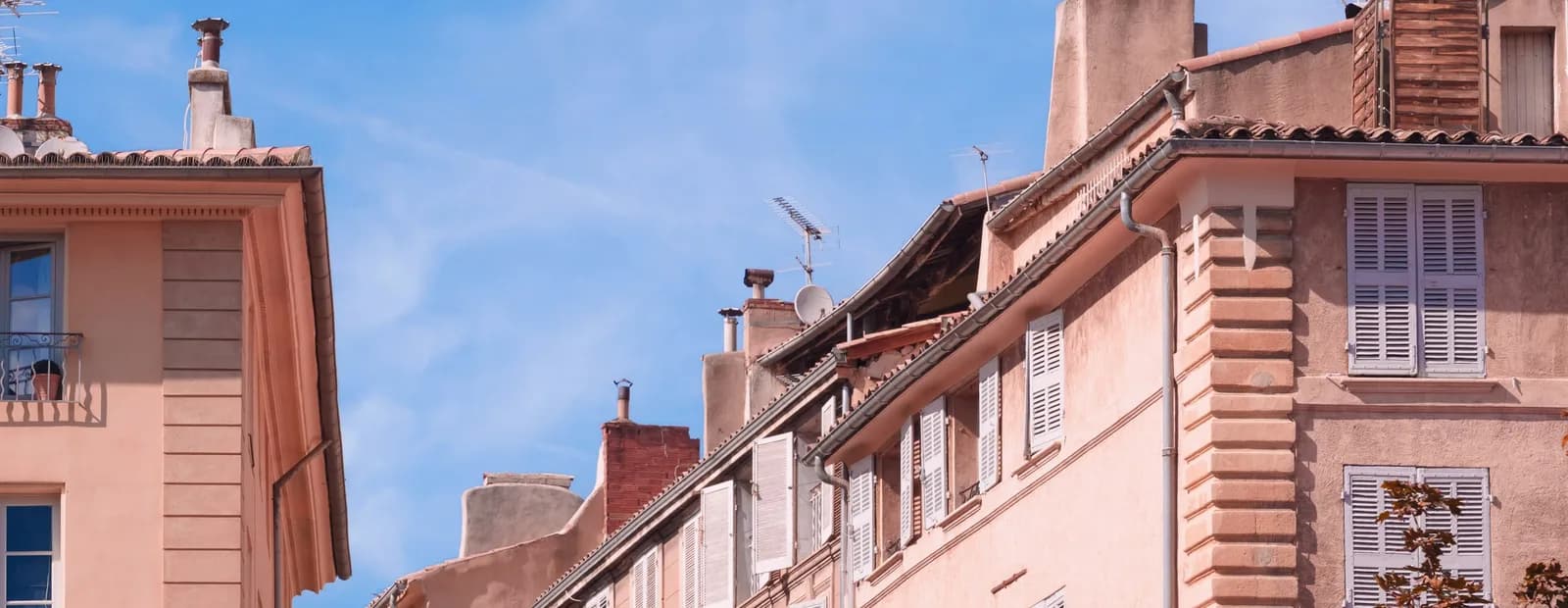 Façades roses aux volets clairs d’une rue du centre d’Aix-en-Provence, sous un ciel bleu traversé de nuages légers.