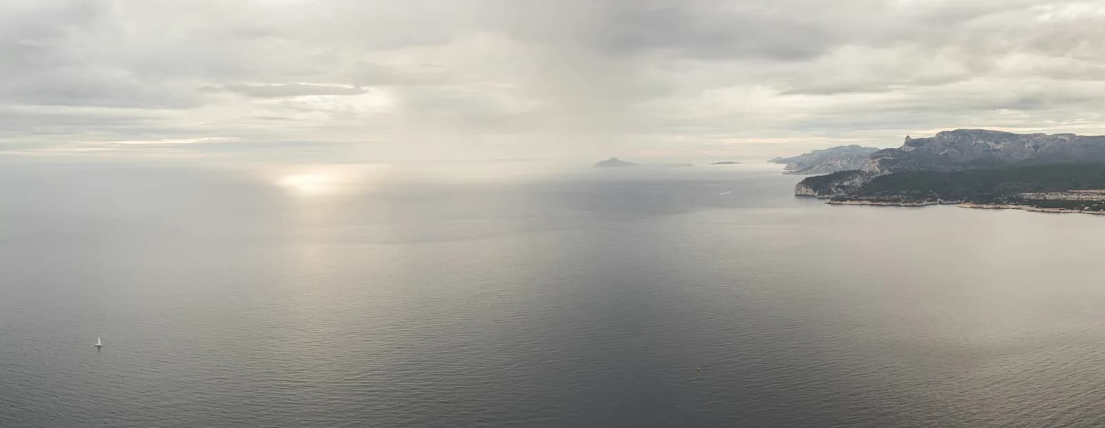 La Méditerranée vue du sommet du cap Canaille, falaise voisine de La Ciotat : mer argentée sous un ciel voilé et côte des calanques au loin.