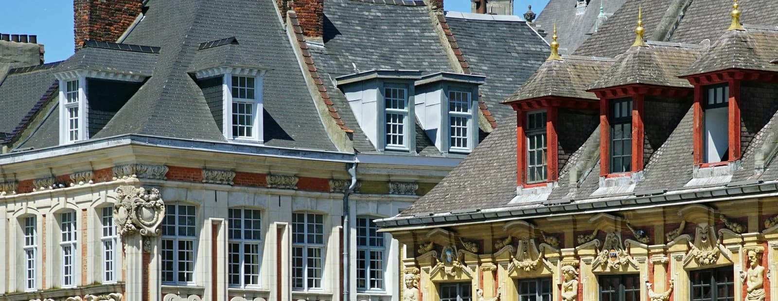 Toitures d’ardoise, lucarnes et façades sculptées de style baroque flamand du centre historique de Lille, sous un ciel bleu d’été.
