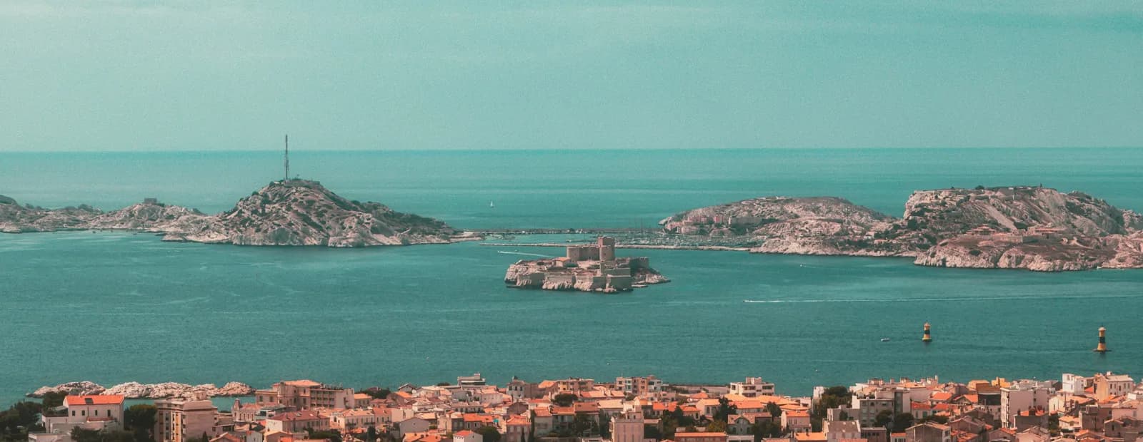 La rade de Marseille vue des hauteurs : l’archipel du Frioul et le château d’If sur une mer turquoise, les toits de la ville au premier plan.
