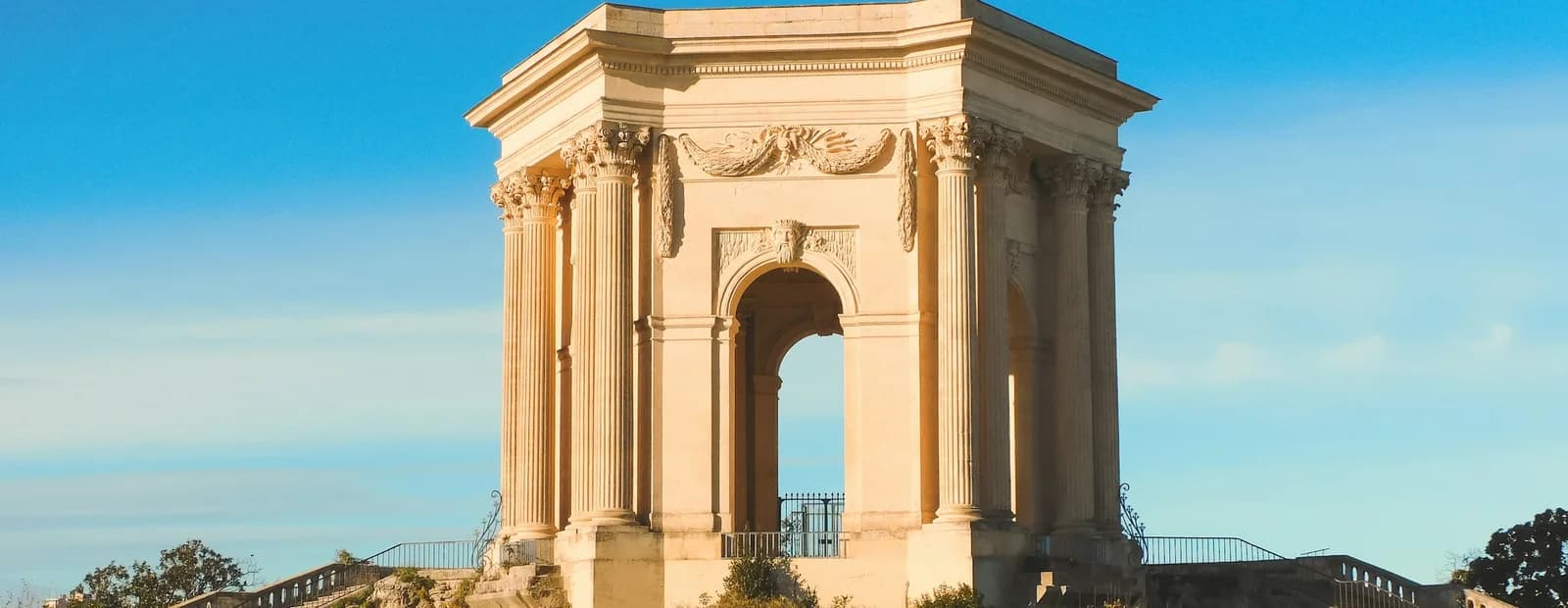 Le château d’eau de la promenade du Peyrou à Montpellier, temple à colonnes en pierre claire, sous un ciel bleu intense.