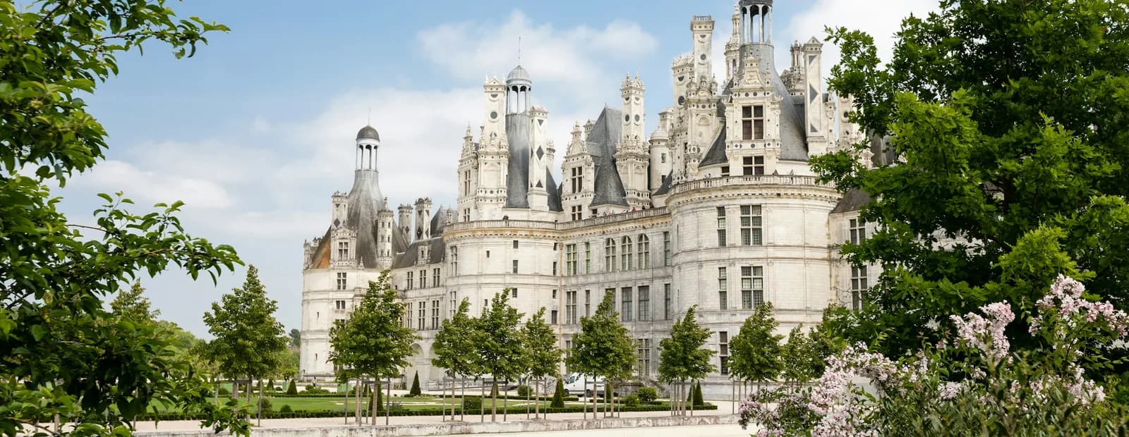 Façade Renaissance en pierre blanche d’un château de la Loire, avec tours et lucarnes, entre arbres et pelouse sous un ciel bleu
