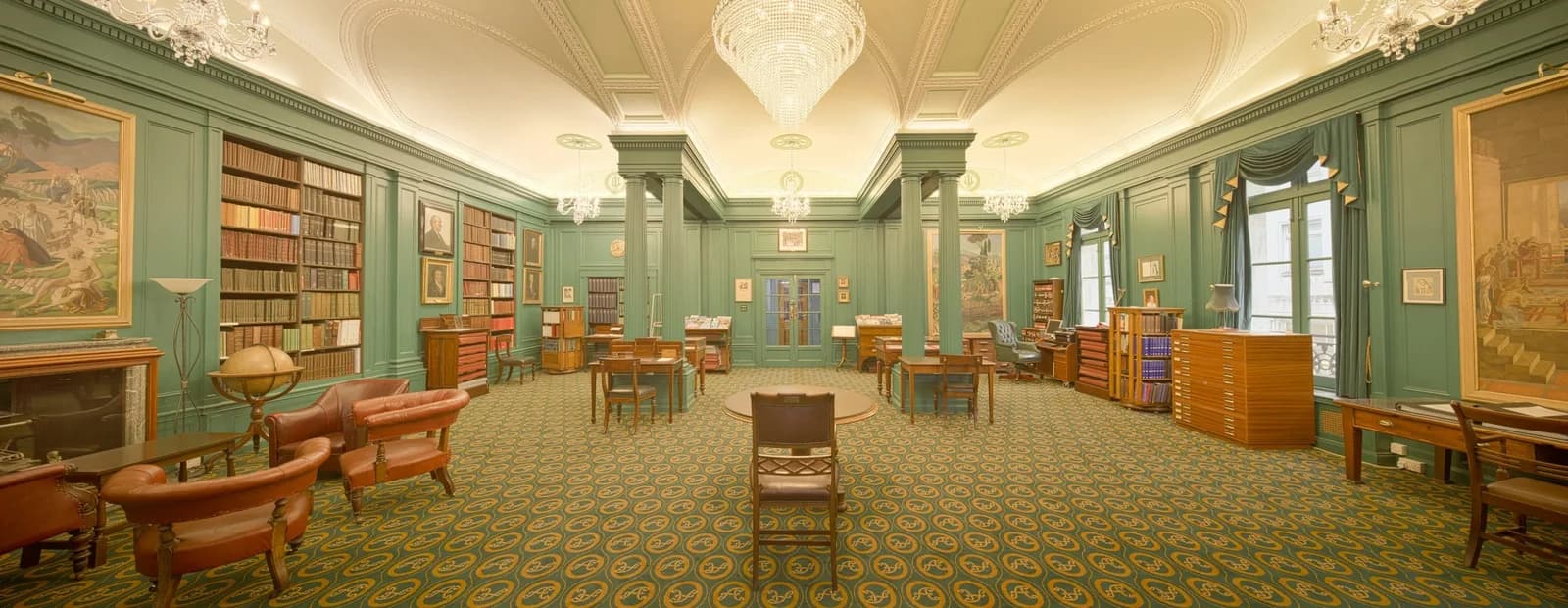 Salon-bibliothèque classique aux boiseries vert céladon, avec lustres en cristal, rayonnages de livres et fauteuils en cuir.