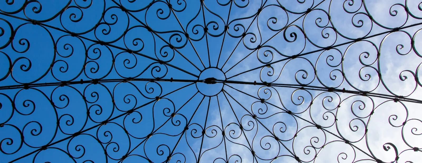 Dôme de fer forgé à volutes vu en contre-plongée, sur un ciel bleu