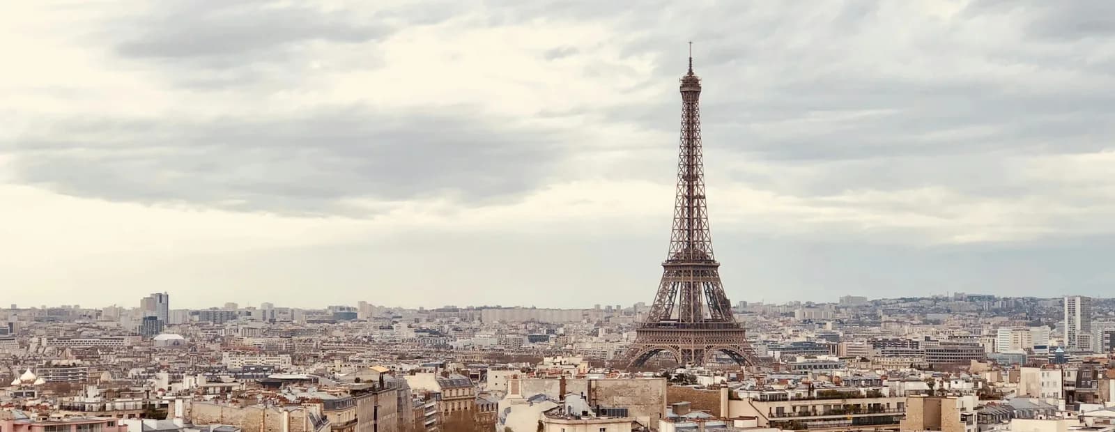 La tour Eiffel dominant les toits haussmanniens de Paris sous un ciel nuageux, vue depuis le sommet de l’Arc de Triomphe.