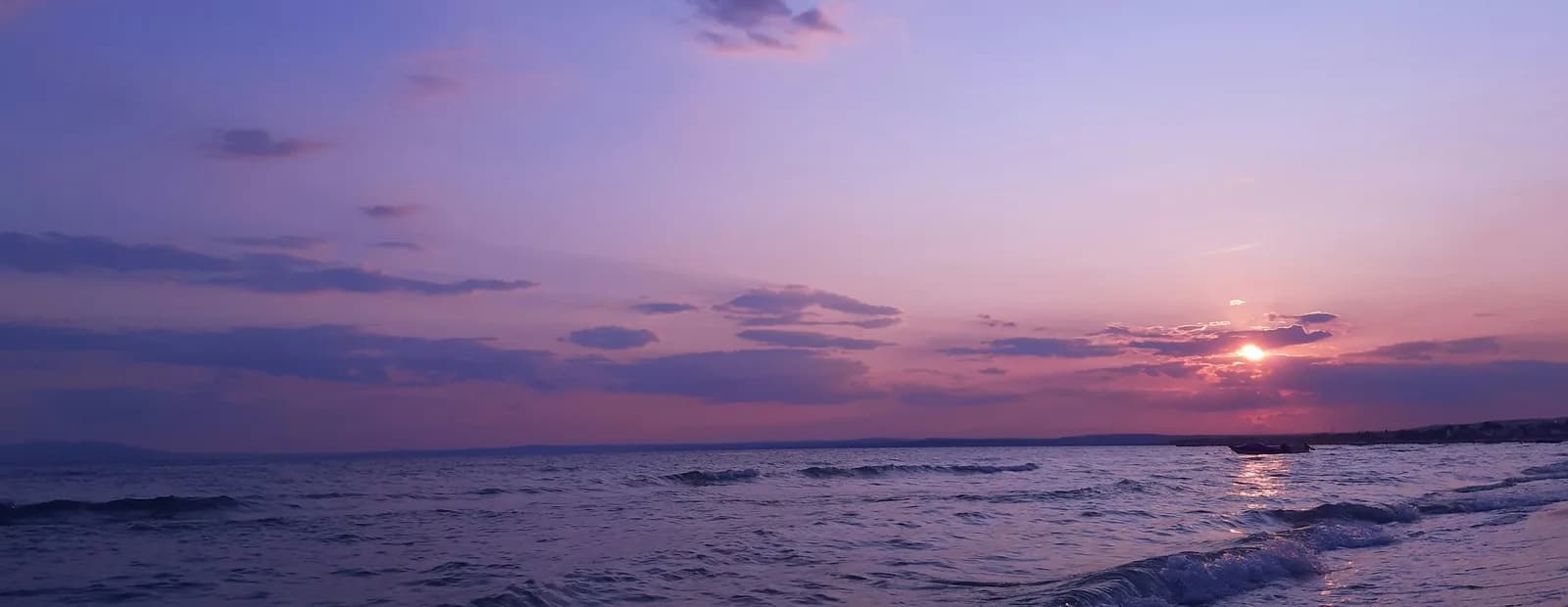 Vagues déferlant sur une plage au coucher du soleil, sous un ciel mauve et bleu traversé de nuages