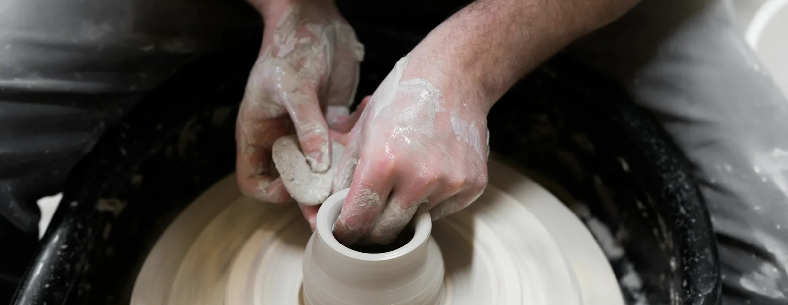 Mains d’un potier façonnant un bol en argile sur un tour, dans un atelier baigné de lumière.
