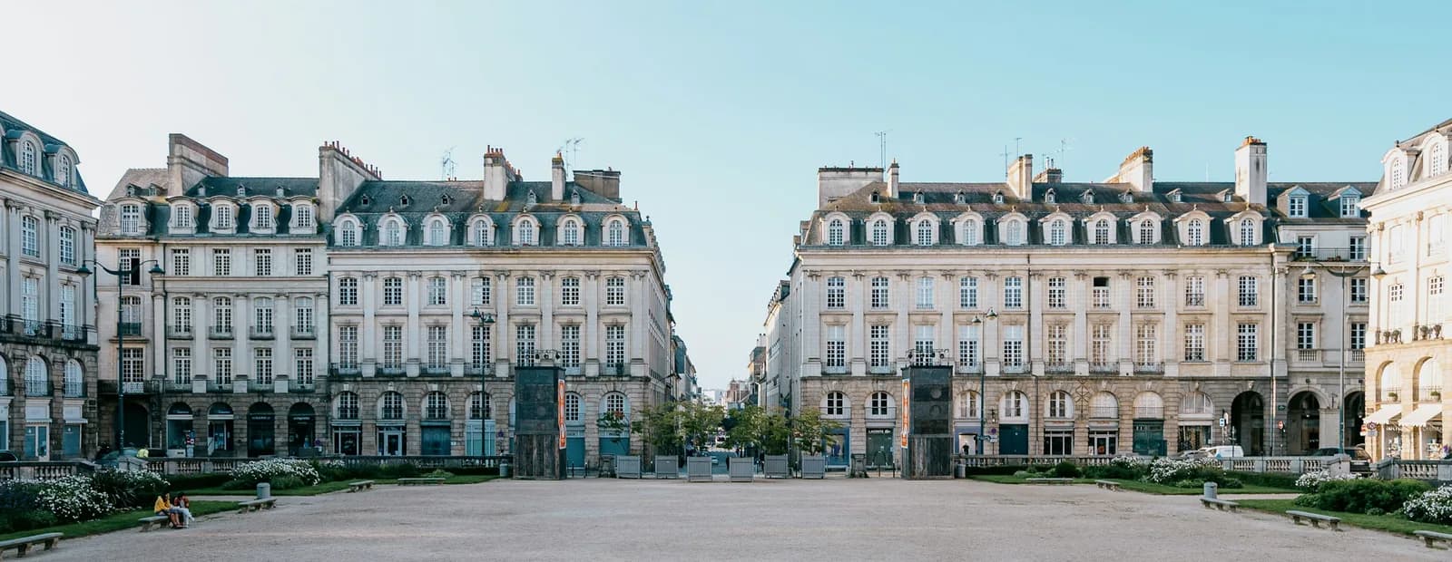 Les façades classiques en granit et tuffeau de la place du Parlement-de-Bretagne à Rennes, sous un ciel bleu pâle et dégagé.