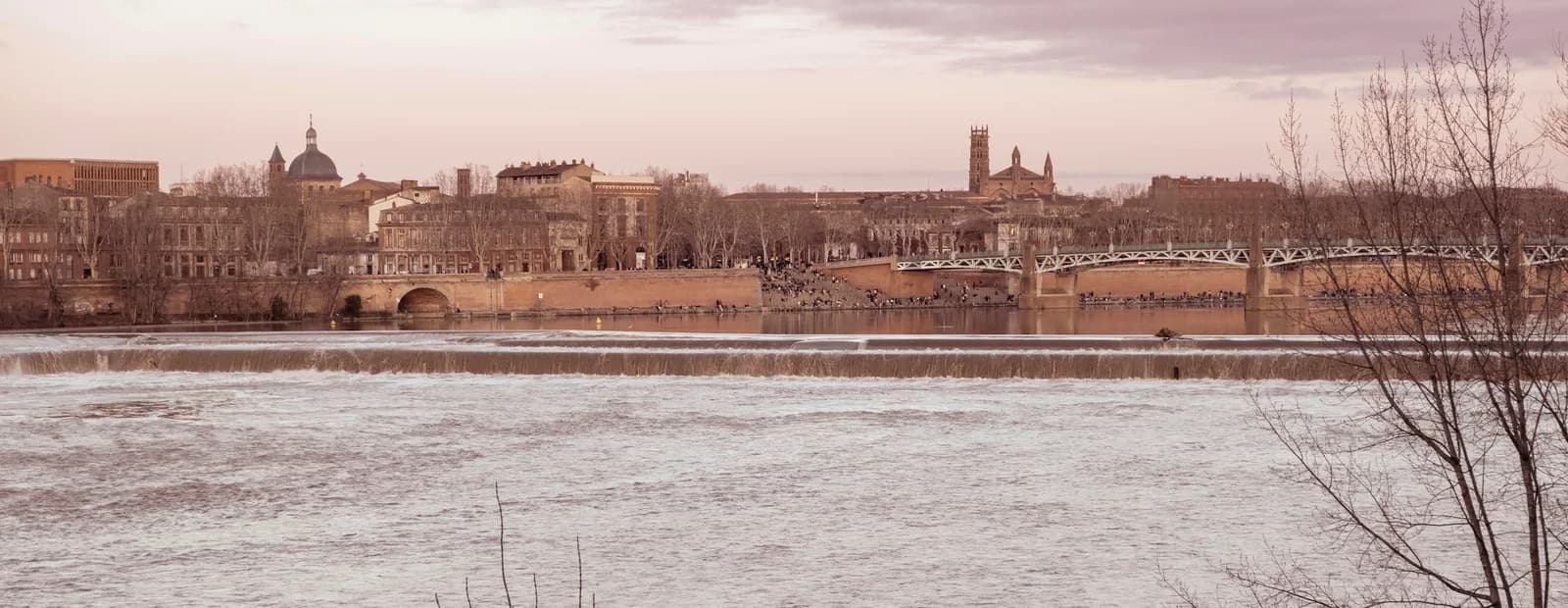La Garonne à Toulouse, sa chaussée et le pont Saint-Pierre devant les quais de brique et le dôme de la Grave, sous un ciel pâle.