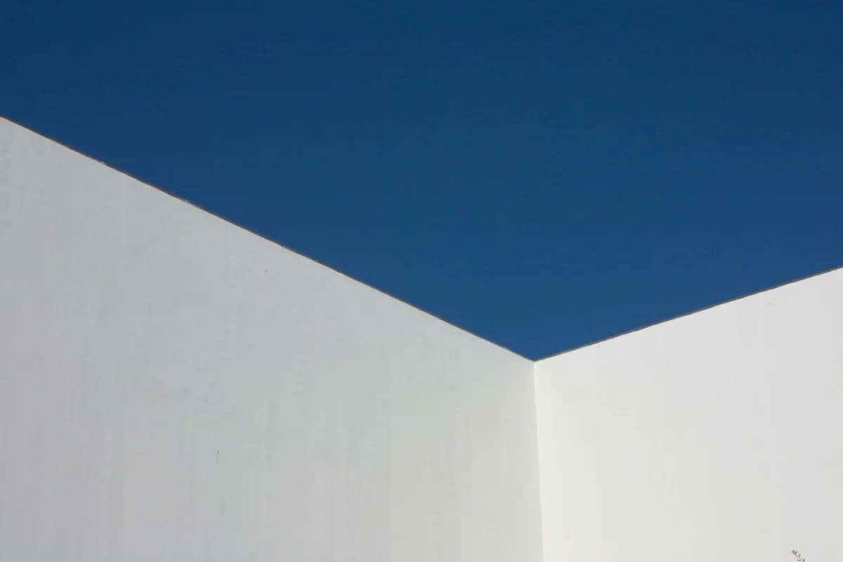 Angle de deux murs blancs lisses se découpant en lignes droites et nettes sur un ciel bleu profond sans nuage.