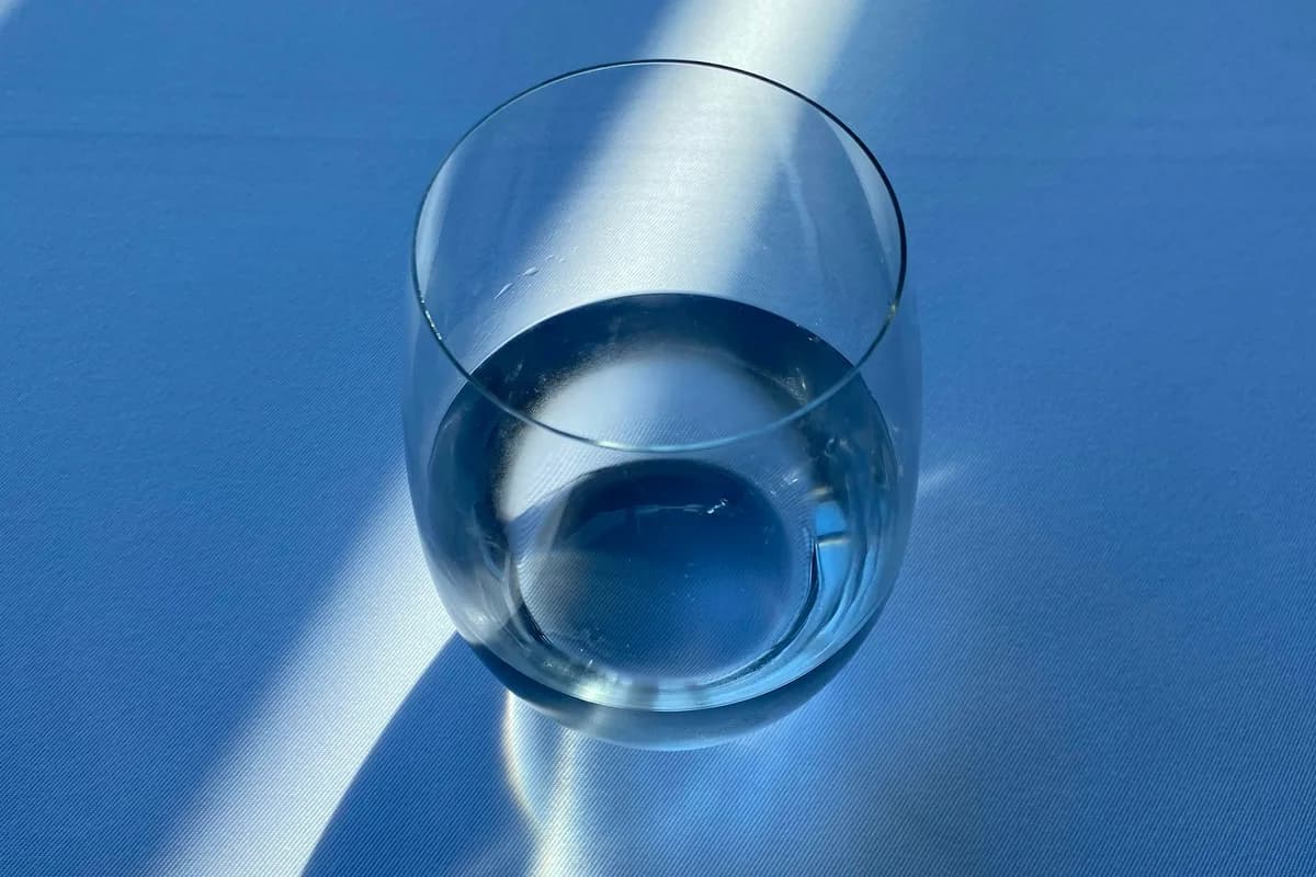 Verre d’eau limpide posé sur une nappe bleue, traversé par des rayons de soleil qui dessinent des bandes de lumière autour de lui.